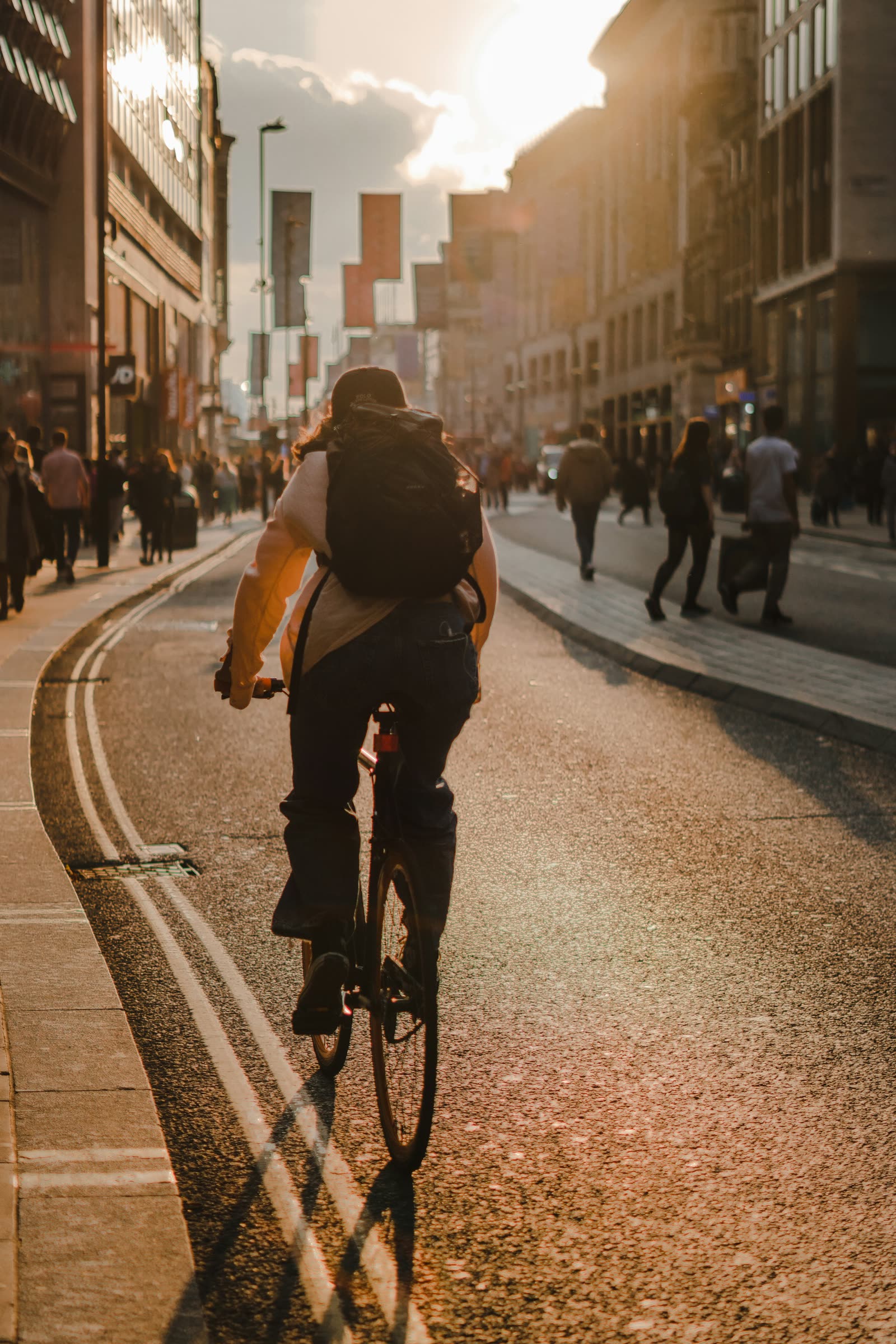 Ciclista com mochila pedalando numa rua movimentada da cidade