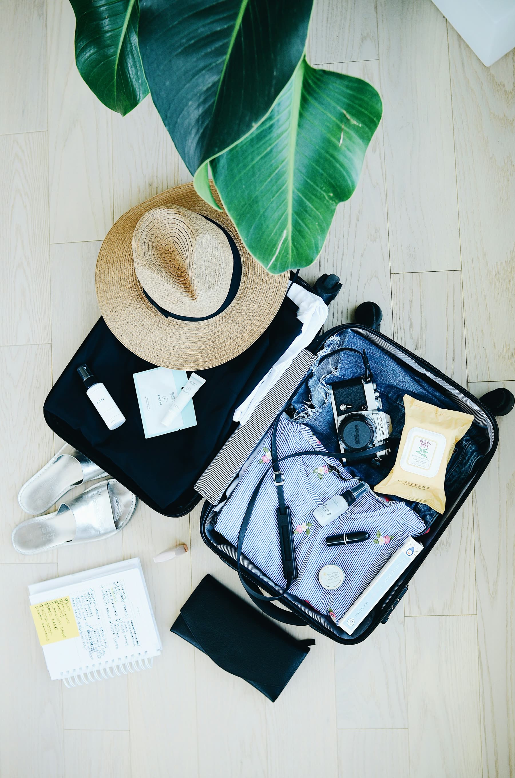 Mala de viagem aberta com chapéu, câmera e itens essenciais
